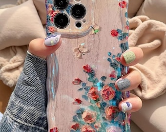 以下が含まれることがあります： 波状の縁取りデザインが施された透明なスマートフォンケース。ピンクと赤のバラ、緑の葉、小さな蝶の模様がプリントされています。ケースにはトリプルレンズカメラシステム用の切り抜きがあり、背景には明るい木目調のテクスチャが施されています。