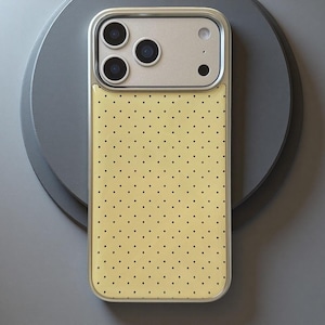 May include: A rectangular smartphone case featuring a pale yellow back panel with a repeating pattern of small black polka dots. The upper section of the case is silver-toned and includes cutouts for a triple-lens camera system and a flash.