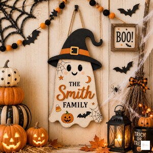 May include: A wooden wall hanging shaped like a ghost wearing a black witch hat with an orange band. The ghost features the text "THE Smith FAMILY" in orange and black, decorated with small pumpkins, bats, stars, and spider web illustrations.