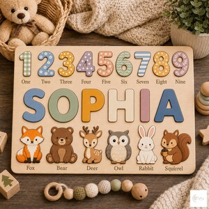 May include: A wooden puzzle board featuring the name SOPHIA in large, colorful letters. Above the name are numbers one through nine with various patterns. Below the name are illustrations of a fox, bear, deer, owl, rabbit, and squirrel with labels.