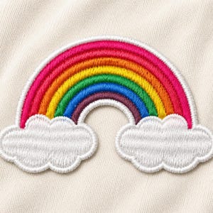 May include: An embroidered patch featuring a colorful rainbow arching over two white clouds. The rainbow consists of distinct bands of pink, orange, yellow, green, blue, and purple thread. The patch is set against a light cream fabric background.