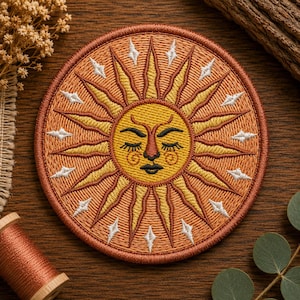 Puede incluir: Un parche bordado circular que presenta un sol estilizado con rostro. El sol tiene los ojos cerrados, nariz y boca, realizados en hilo amarillo y marrón oscuro. Está rodeado por rayos alternos amarillos y naranjas y pequeños detalles de estrellas.