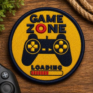 Puede incluir: Un parche bordado circular con fondo amarillo y borde azul oscuro. Presenta el texto "GAME ZONE" en azul oscuro, con una "O" roja. Debajo hay un gráfico de mando de juego azul oscuro, la palabra "LOADING" y una barra de carga roja.