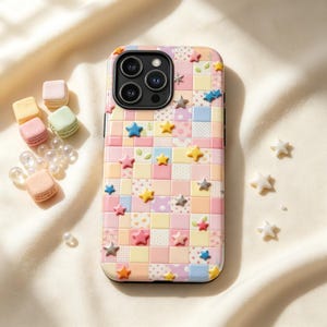 Op de afbeelding: Een smartphonehoesje met een pastelkleurig ruitpatroon in tinten roze, geel, blauw en wit, versierd met kleine driedimensionale stervormige bedeltjes in diverse kleuren, naast verschillende kleine pastelkleurige macarons en witte parels.