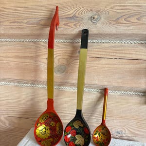 Könnte beinhalten: Drei Holzkellen in verschiedenen Größen mit handgemalten Blumenmustern in Rot, Schwarz und Gold. Die größte Kelle hat einen Haken am Griff, die mittlere einen schwarzen Griff und die kleinste einen roten Griff mit goldenen Akzenten.