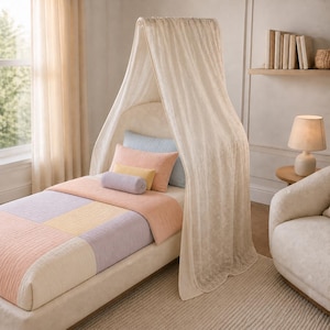 May include: A twin bed with a beige upholstered headboard and a canopy draped in a cream-colored fabric. The bedding features a quilted patchwork design in soft shades of peach, yellow, and lavender, complemented by a matching bolster pillow.
