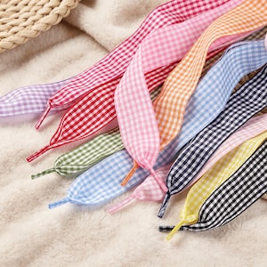 Könnte beinhalten: Eine Sammlung flacher Schnürsenkel mit Vichy-Karo-Muster in verschiedenen Farben, darunter Rot, Rosa, Orange, Hellblau, Dunkelblau, Gelb, Schwarz, Grün und Violett, jeweils mit einer passenden Kunststoffspitze am Ende versehen.