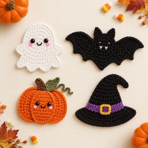 Könnte beinhalten: Vier gehäkelte Halloween-Dekorationen, bestehend aus einem weißen Geist mit rosa Wangen, einer schwarzen Fledermaus mit weißen Fangzähnen, einem orangefarbenen Kürbis mit grünem Stiel und Blatt sowie einem schwarzen Hexenhut mit violettem Band.