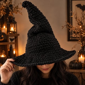 May include: A black crocheted witch hat with a tall, pointed crown and a wide, circular brim. The hat is constructed from thick, textured yarn with a visible knotted stitch pattern throughout, creating a dense and structured appearance.