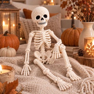 Op de afbeelding: Een gehaakt skeletfiguur gemaakt van gebroken wit garen met zwarte garendetails voor de oogkassen en tanden. Het figuur heeft een gedetailleerde ribbenkast, beweegbare ledematen en een ronde schedel, opgebouwd met zichtbare steken.