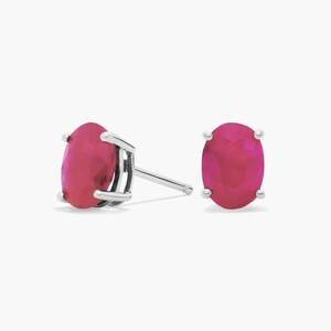 Könnte beinhalten: Ein Paar Ohrstecker mit oval geschliffenen, leuchtend pinken Edelsteinen in poliertem, silberfarbenem Metall. Jeder Ohrstecker ist mit einer Vier-Krappen-Fassung versehen, die die facettierte Oberfläche der Steine und den Metallstift zeigt.