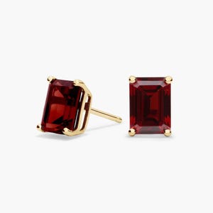 Puede incluir: Un par de pendientes de botón con piedras preciosas de granate rojo intenso de corte esmeralda rectangular engastadas en oro amarillo pulido. Cada pendiente se asegura con un poste de oro y cuatro garras que sujetan la piedra.