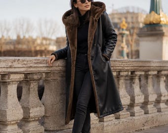 May include: A long black coat with a brown faux fur lining and a large hood, worn over a black turtleneck sweater and black trousers. The outfit is completed with black pointed-toe ankle boots and dark-tinted sunglasses, creating a cohesive look.
