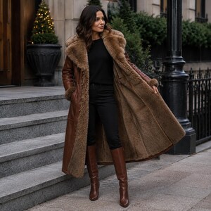 May include: A long brown leather coat with a thick tan faux fur lining and wide lapels, worn over a black long-sleeve top and black trousers, paired with knee-high brown leather boots. The coat features a button closure and visible fur trim.