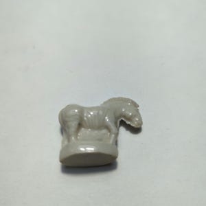 May include: A white ceramic figurine of a zebra standing on a base. The zebra has black stripes and is facing to the right.