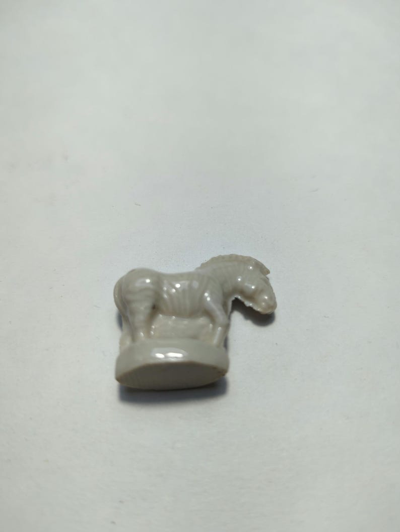May include: A white ceramic figurine of a zebra standing on a base. The zebra has black stripes and is facing to the right.
