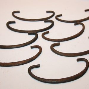 May include: Ten rusty metal C-shaped hooks. The hooks are all the same size and shape, and they are arranged in a random pattern on a white background.
