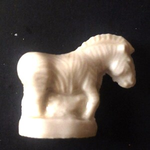 May include: A white ceramic figurine of a zebra with a striped pattern. The zebra is standing on a base and has a small foal beside it.