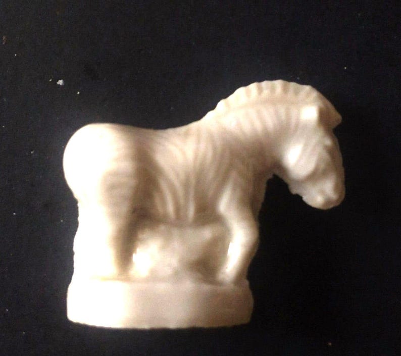 May include: A white ceramic figurine of a zebra with a striped pattern. The zebra is standing on a base and has a small foal beside it.