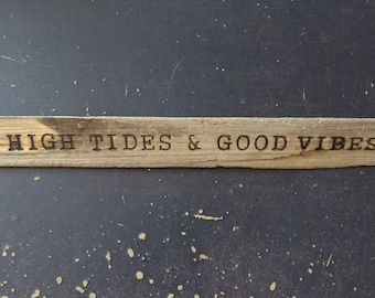 May include: A piece of driftwood with the words "High Tides & Good Vibes" burned into the surface.
