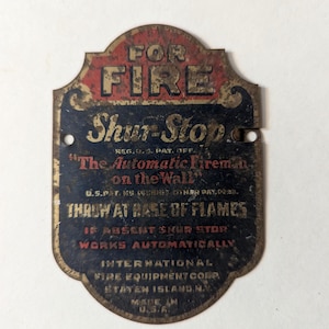 Peut inclure: Panneau métallique vintage rouge et noir avec l'inscription « FOR FIRE » en haut. Le panneau indique « Shur-Stop » et « The Automatic Fireman on the Wall ». Il comprend également le texte « THROW AT BASE OF FLAMES » et « MADE IN U.S.A. »