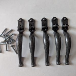 May include: Five antique silver cabinet door pulls with a decorative design. The pulls are all the same size and shape, and they have a slightly curved handle. The pulls are arranged in a row, and they are all facing the same direction.