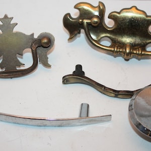 May include: Five different cabinet knobs and pulls in various styles and finishes.  Two are ornate brass with a leaf design, one is a simple silver curved pull, one is a silver knob with a ridged design, and one is a silver pull with a curved shape.