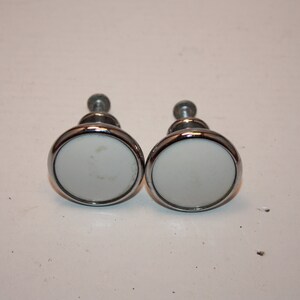May include: Two round, white ceramic cabinet knobs with a silver metal rim and screw.