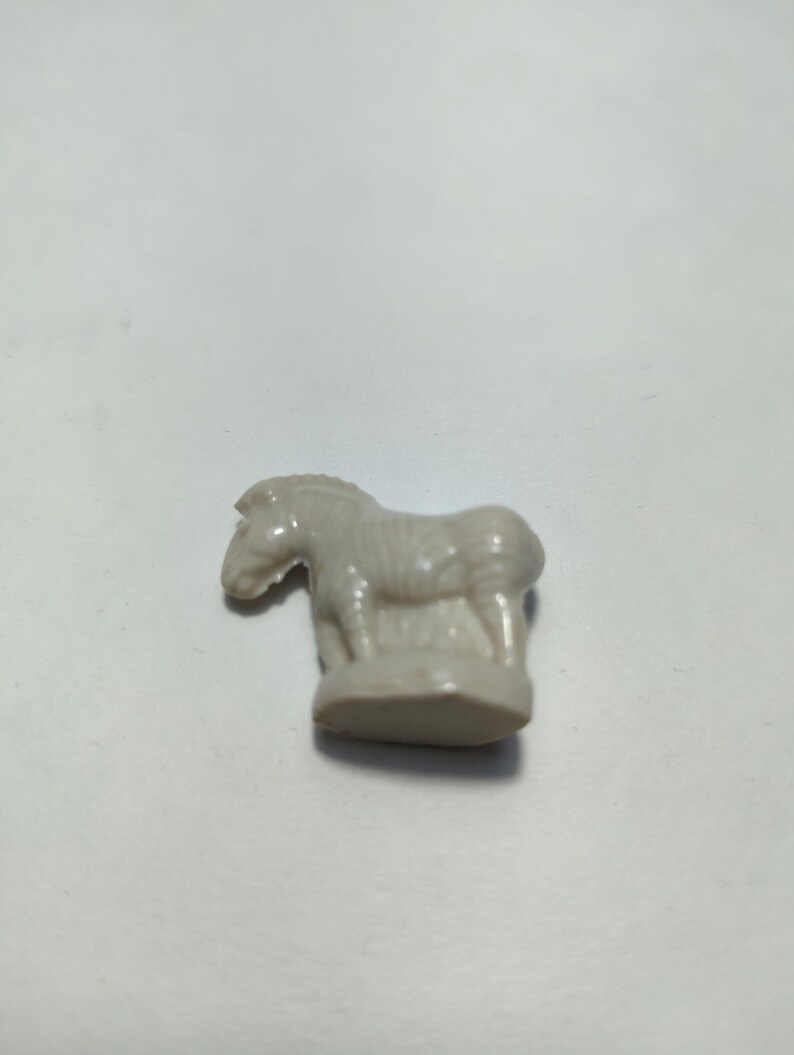 May include: A white ceramic figurine of a zebra standing on a base. The zebra has black stripes and a detailed face.