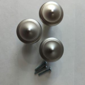 May include: Three silver-toned metal finials with a rounded top and a raised ring around the base. The finials are accompanied by four silver-toned screws.