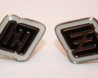 May include: A pair of silver cufflinks with a black and white geometric design. The design is a stylized letter "E" in a square shape.