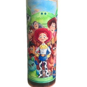 May include: A cylindrical metal tumbler featuring a colorful, wrap-around graphic print of various animated characters from the Toy Story franchise, including a central cowgirl figure, a cowboy, a potato-shaped character, and a green alien.