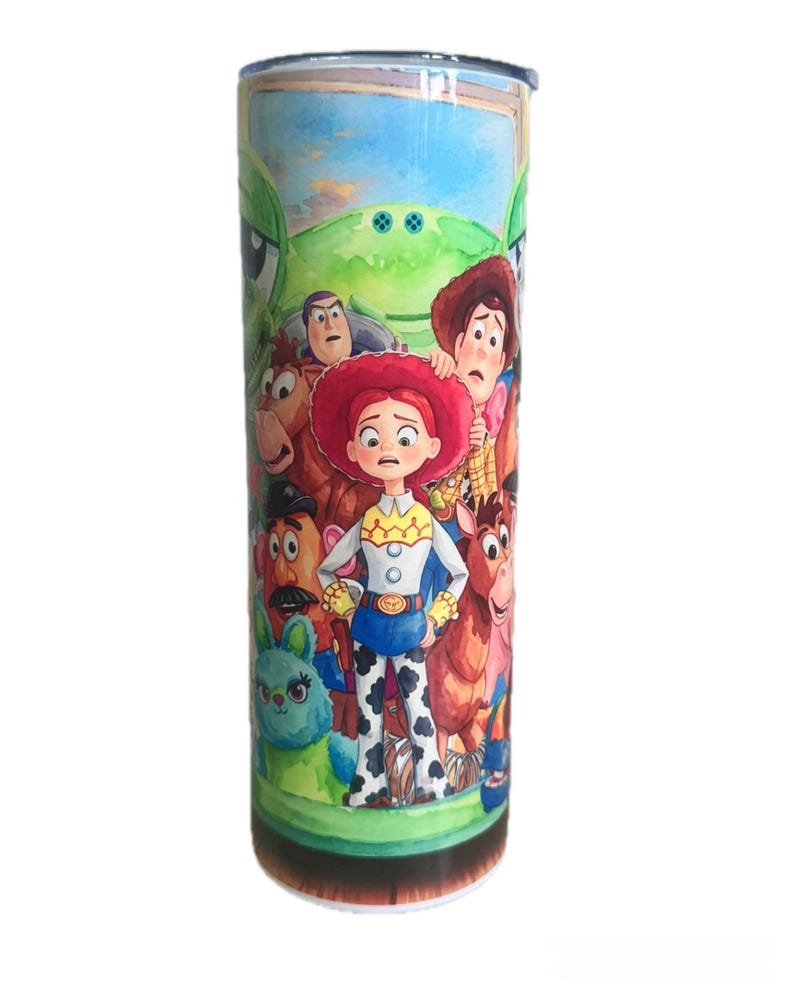 May include: A cylindrical metal tumbler featuring a colorful, wrap-around graphic print of various animated characters from the Toy Story franchise, including a central cowgirl figure, a cowboy, a potato-shaped character, and a green alien.