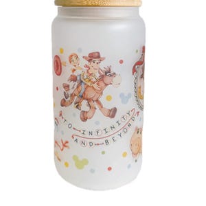 May include: A frosted glass tumbler with a bamboo lid and a clear straw, featuring a colorful wrap-around print of cartoon characters riding a horse, accompanied by the text TO INFINITY AND BEYOND, interspersed with small multi-colored polka dots.