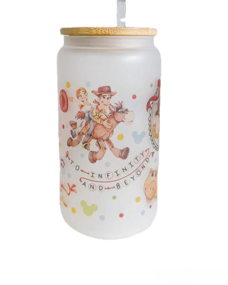 May include: A frosted glass tumbler with a bamboo lid and a clear straw, featuring a colorful wrap-around print of cartoon characters riding a horse, accompanied by the text TO INFINITY AND BEYOND, interspersed with small multi-colored polka dots.