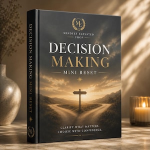 Op de afbeelding: Een zwart hardcover boek getiteld Decision Making Mini Reset van Mindset Elevated Shop. De kaft toont een gouden zonsondergang boven een splitsing in een zandpad met een wegwijzer, en de tekst Clarify what matters. Choose with confidence.
