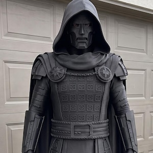 May include: A full-body matte black costume featuring a hooded cloak, a rigid mask with a stern expression, a textured chest plate with a grid pattern, shoulder pauldrons, gauntlets, a wide belt, and armored leg guards covering the boots.