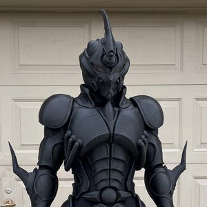 May include: A full-body matte black armored suit featuring a helmet with a prominent central horn, sculpted chest plating, shoulder guards, and pointed forearm extensions. The suit has a segmented, insect-like design with detailed armor plating.