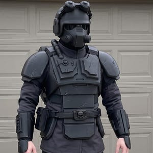 May include: A full-body black tactical costume featuring a helmet with goggles and a respirator, a chest plate with shoulder guards, forearm bracers, a utility belt, and leg armor covering the thighs and shins, worn over a dark long-sleeved uniform.