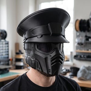 May include: A matte black tactical helmet featuring a wide brimmed officer-style cap top integrated with a full-face protective mask. The mask includes a dark tinted visor and a vented lower section with horizontal slats for a structured appearance.