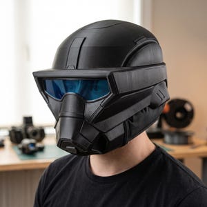 May include: A matte black full-face helmet featuring a prominent angular visor with a reflective blue tint. The helmet has a structured, multi-paneled design with visible 3D-printed layer lines across the surface and a wide, protruding brow section.