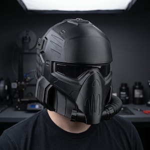 May include: A matte black full-face helmet featuring a textured 3D-printed finish, a wide horizontal visor, and a prominent respirator-style mouthpiece with a flexible tube attachment extending from the lower right side of the protective shell.