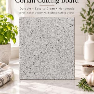 May include: A square Corian cutting board with a light gray speckled terrazzo-like pattern. The text above reads: Corian Cutting Board, Durable, Easy to Clean, Handmade, DuPont Corian Custom Antibacterial Cutting Boards. The board is solid.