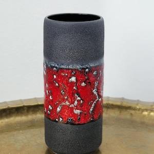 Puede incluir: Un jarrón cilíndrico de cerámica con un acabado negro mate texturizado en las secciones superior e inferior, contrastado por una ancha banda central de color rojo vibrante con un patrón de esmalte grueso, elevado y moteado en blanco y negro.