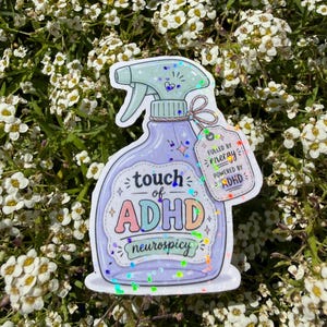 May include: A holographic sticker shaped like a purple spray bottle with a light green nozzle. The label reads "touch of ADHD" and "neurospicy" with a small tag attached that says "FULLED BY energy POWERED BY ADHD" in colourful lettering.