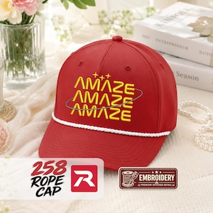 May include: A red baseball cap featuring a white rope trim across the base of the crown. The front displays the word AMAZE embroidered in yellow three times, stacked vertically, with three small yellow stars above and a thin grey orbital ring.