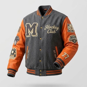 Peut inclure: Une veste universitaire en mélange de laine grise avec des manches en cuir orange, arborant une grande lettre M, le texte Hockey Club et Est. 2010. Les manches sont ornées de divers écussons brodés, dont un casque de hockey et le nombre 77.