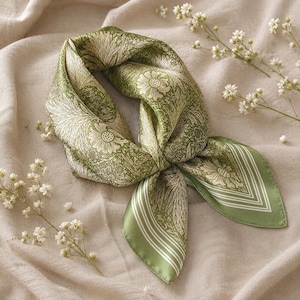 May include: A square scarf featuring a sage green and cream floral pattern with intricate botanical illustrations of flowers and leaves. The scarf has a smooth, satin-like finish and is folded into a knot, displaying a border with thin white stripes.