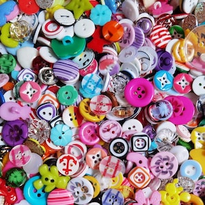 Puede incluir: Una gran colección de botones de costura surtidos en varias formas, tamaños y colores, incluyendo diseños redondos, cuadrados y en forma de estrella, con patrones como rayas, cuadros y un icono de ancla, con acabados translúcidos y sólidos.