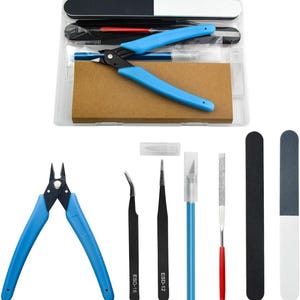 May include: A model building tool kit containing a pair of blue side cutters, two black tweezers labeled ESD-15 and ESD-12, a blue hobby knife with a cap, a metal file with a red handle, and two rectangular sanding sticks in black and white.